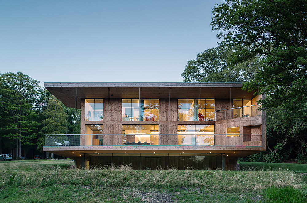 The new build house replaces an existing 1920s summer house in an area of woodland overlooking a stream and farmland beyond. Clad in corten steel panels and timber, the house is arranged over three levels with the main living spaces accessed via a folded steel plate bridge leading out to a veranda. Solid oak stairs are machined from timber from the woods and cantilevered from the supporting insitu concrete walls leading either up to the bedrooms or down to the swimming pool where the timber-framed glass panels open to the surrounding meadow. We provided all mechanical and electrical services including drainage, utilities and design of the dual fuel biomass boiler system, control strategy and its interface with an auxiliary LPG heating system. A sedum-planted green roof references the woodland floor while collecting and harvesting rainwater.