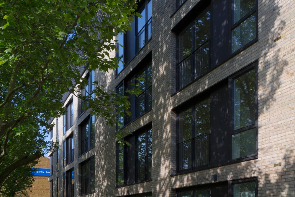 The design addressed the split nature of the site to create a linear building with opposing faces. Apartments face south onto an enclosed residential green space and are clad with a punched brick facade of domestic scale. The north facing circulation spaces buffer the apartments from the railway viaduct and are shrouded in a protective expanded metal skin.