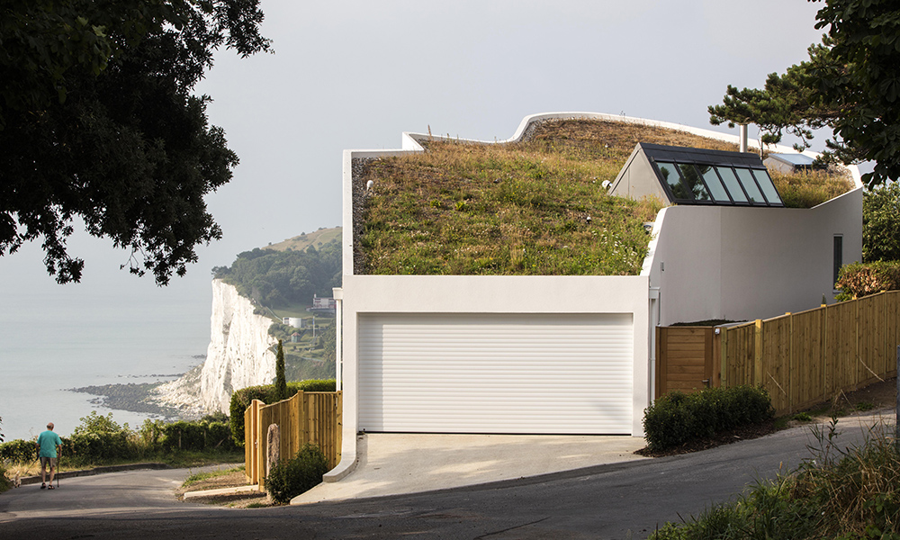 Ness Point house is a new family house built on an exposed clifftop, 65 metres above the sea on the white cliffs of Dover. The undulating form of the plan orientates the internal spaces to different aspects of the landscape beyond. The sea-facing facade orients large windows in opposing directions to take in views of the coastline, including Ness Point, the most easterly part of the British Isles. The highly sealed and insulated house utilises heat recovery and solar thermal renewable systems to maximise energy efficiency in the winter, whilst the long gallery skylight and eco-vents enable controlled passive cooling in the summer. The bio-diverse green roof helps retain rainwater and harbour local wildlife while helping merge the house into the landscape. We provided all mechanical, electrical and sustainability services.