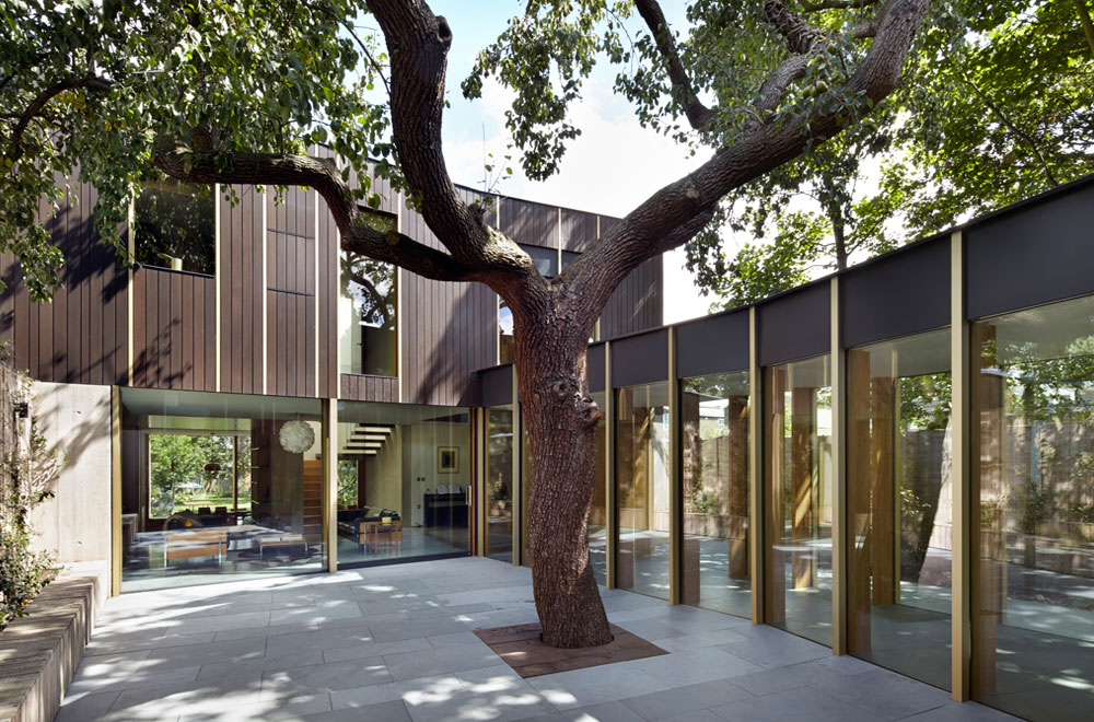 The pear tree house is built around a 100-year-old pear tree, a remnant of the site’s history as a Victorian fruit orchard. The house is built around the tree in two volumes and linked by a glass walkway. Board marked concrete to the ground floor walls support a timber box at first floor, with openings framed by gold aluminium trims. The lower portion of each block is made from a combination of woodgrain-imprinted concrete and glass. The larch formwork used to create the concrete walls is reused as cladding for the timber-framed upper storeys.