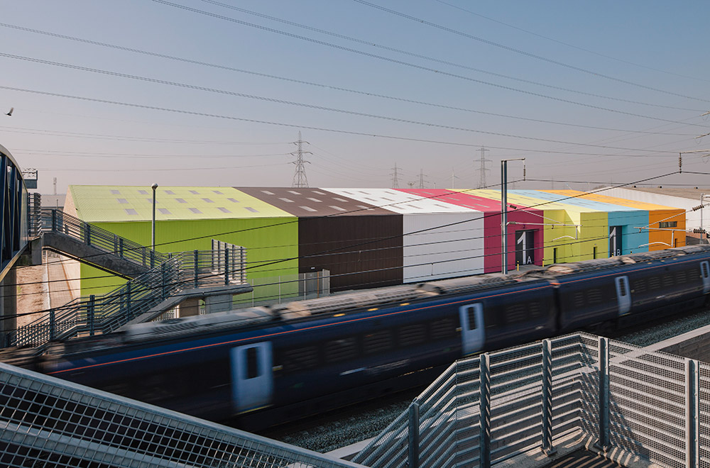 The warehouse refurbishment is a 200m long ‘supershed’ containing five 800m² standalone business units with individual service yards, loading bay access and cores. The new building incorporates the reuse of the original slab and frame, a new sustainably insulated roof and a multicoloured cladding system. Responding to both the scale of the building and its landscape setting at the edge of the marshes, the light industrial building is expressed as 40m wide strips of vibrant colour. We provided all mechanical, electrical and sustainability services including drainage and utilities. The building achieves BREEAM ‘Very Good’ certification.